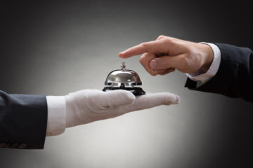 Die Hand eines Butlers reicht einer anderen Hand eine Klingel.