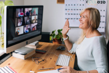 Eine Lehrerin sitzt im Distanzunterricht zu Hause vor ihrem PC und begrüßt ihre Klasse in der Videokonferenz.