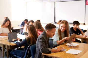 Jugendliche Schüler*innen arbeiten in der Schule mit digitalen Endgeräten zusammen.