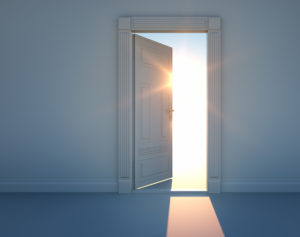 Durch eine geöffnete Tür scheint Sonnenlicht von draußen in einen dunklen Raum hinein.