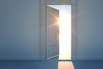 Durch eine geöffnete Tür scheint Sonnenlicht von draußen in einen dunklen Raum hinein.