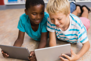 Zwei Jungen liegen bäuchlings auf dem Boden und arbeiten jeweils mit einem Tablet.