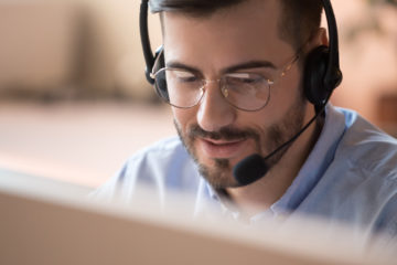 Ein Mann mit Headset sitzt vor einem Computerbildschirm und arbeitet.