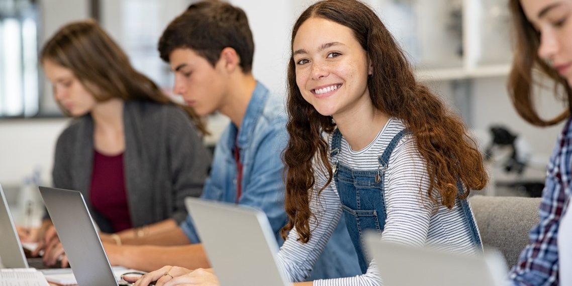 Vier Schüler*innen sitzen in einer Reihe und arbeiten jeweils mit einem Laptop.