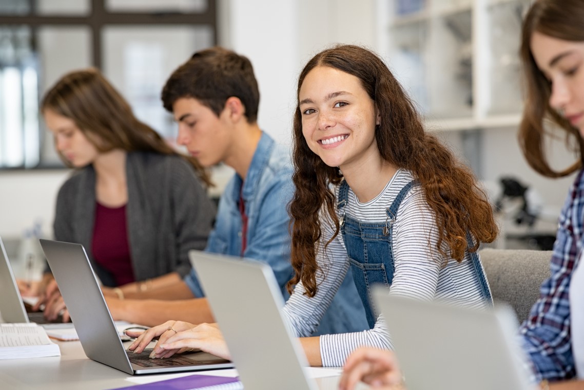 Vier Schüler*innen sitzen in einer Reihe und arbeiten jeweils mit einem Laptop.